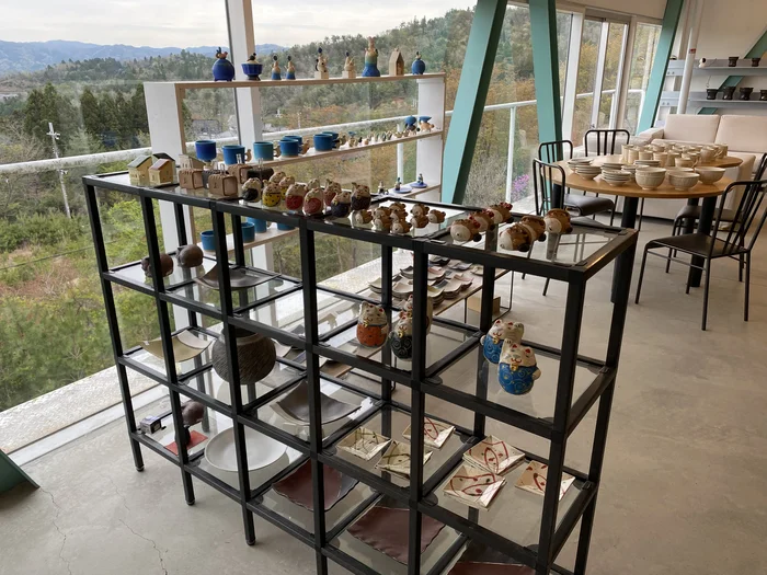 窓際の棚にミニチュア置物が並び、奥にソファ席がある