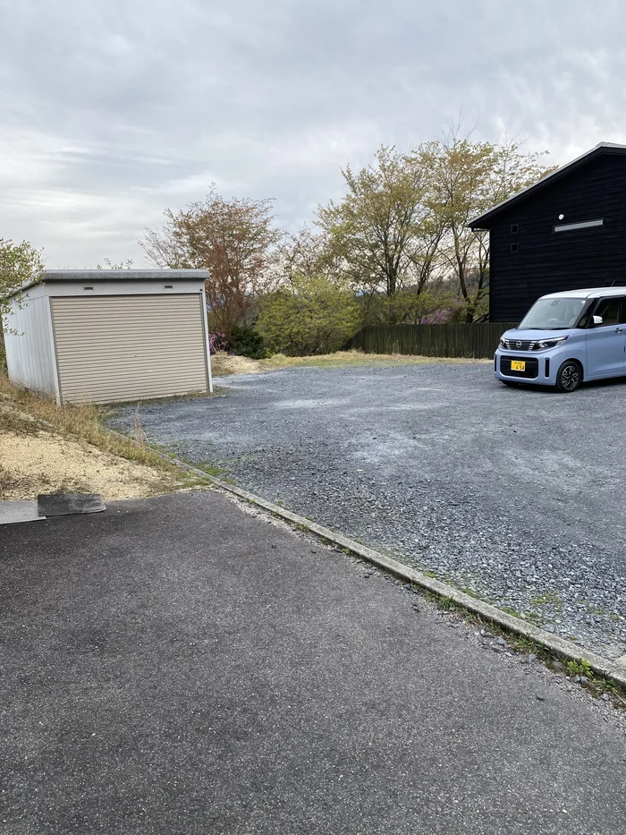 砂利の駐車場と黒い建物、軽自動車が1台停まっている