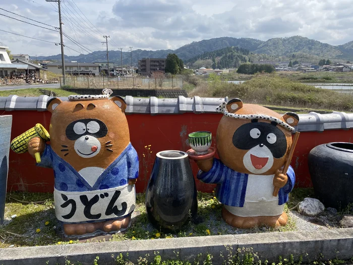 駐車場に立つ「うどん」と書かれた2体の可愛い狸の置物