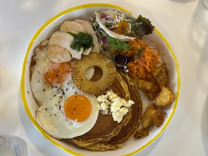 目玉焼きと鶏ハム、パンケーキ、パイナップル、野菜が盛られた朝食プレート