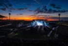 夕暮れの野球場で開催された大規模野外ライブ、照明とスモークに照らされたステージと観客