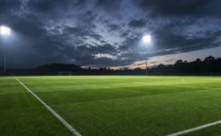 ナイター照明に照らされた無人のサッカーピッチ、夕暮れの曇天を広角でとらえた情景
