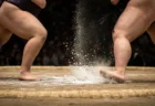 土俵上でぶつかり合う力士の足元と舞い散る塩、低いアングルの近景