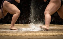 土俵上でぶつかり合う力士の足元と舞い散る塩、低いアングルの近景
