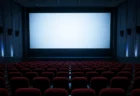 大型スクリーンが淡く光る無人の映画館、赤いシートが並ぶ客席