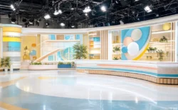朝の情報バラエティー番組を思わせる生放送スタジオのセットと照明を写実的に捉えた情景