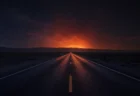 夜の荒野をまっすぐ伸びるハイウェイ、地平線が炎のようなオレンジの光に包まれている