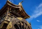 夏の青空の下、金色の装飾が輝く山鉾の屋根と車輪を見上げる写実的な情景