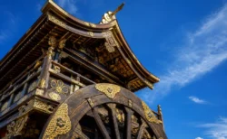 夏の青空の下、金色の装飾が輝く山鉾の屋根と車輪を見上げる写実的な情景