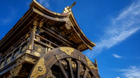 夏の青空の下、金色の装飾が輝く山鉾の屋根と車輪を見上げる写実的な情景