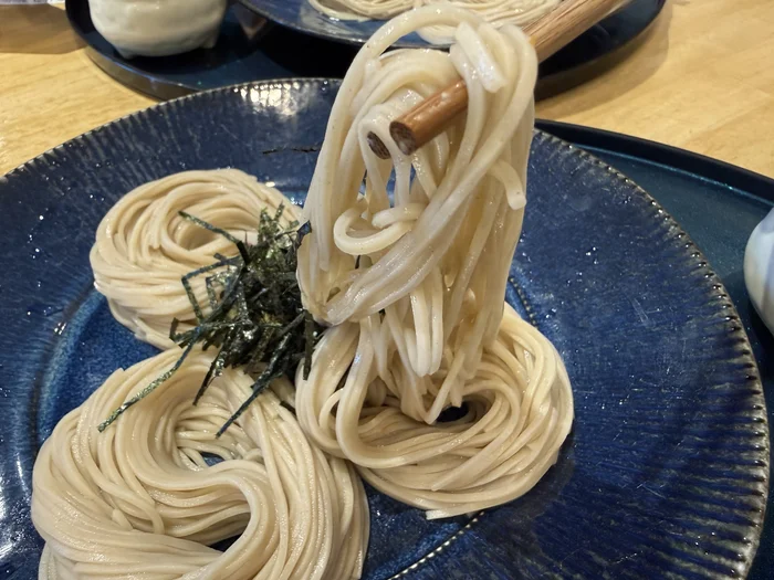 青い皿から箸で持ち上げた細めの冷たい蕎麦