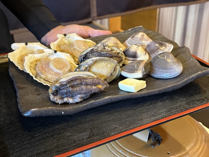 画像 加熱前の浜焼きの食材。帆立・鮑・蛤とバターが黒い皿に並ぶ