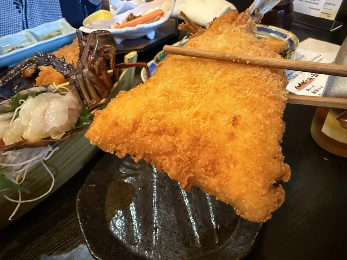 画像 箸で持ち上げたアジフライ。衣の厚みと身の分厚さが分かる