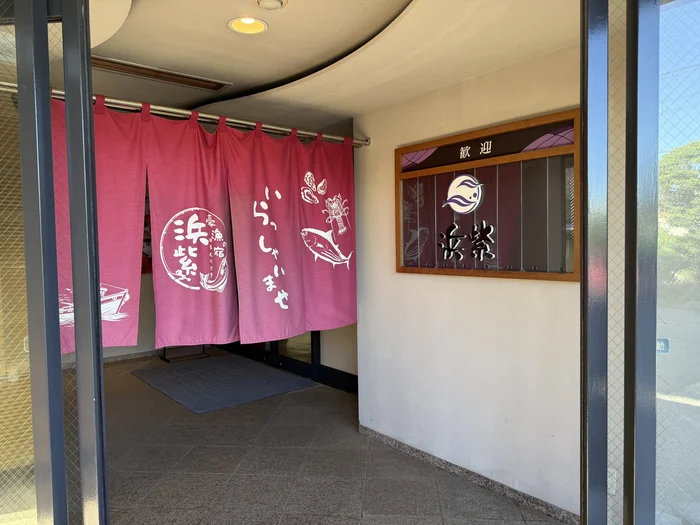 画像 魚や伊勢海老が描かれたピンク色の暖簾がかかる宿の入口