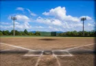 バックネット越しに見る夏の高校野球場のマウンドとホームベース、青空と入道雲
