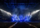 大規模な屋内コンサートアリーナのステージ照明とスモークエフェクトが映える写実的な情景。観客席は無人