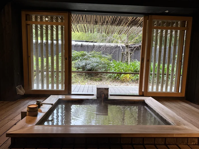 画像 木製の湯船と障子、開け放たれた窓の先に庭が見える客室露天風呂