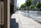 強い日差しで熱気が揺らぐ無人の街路と高温を示す温度計