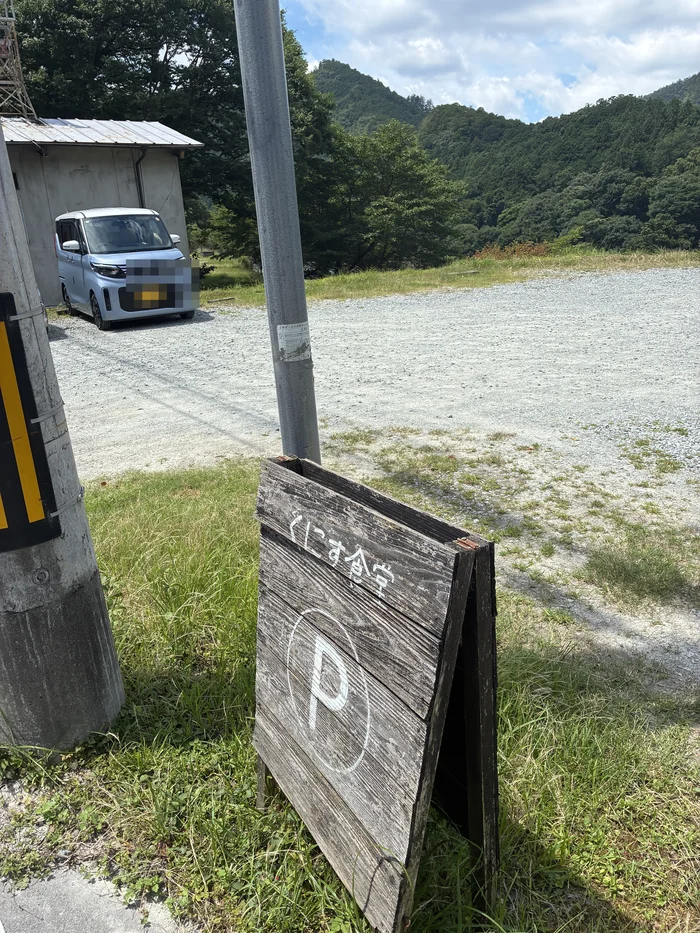 画像 くにす食堂の道路向かいにある砂利の駐車場と案内看板。車のナンバーはモザイク処理済み