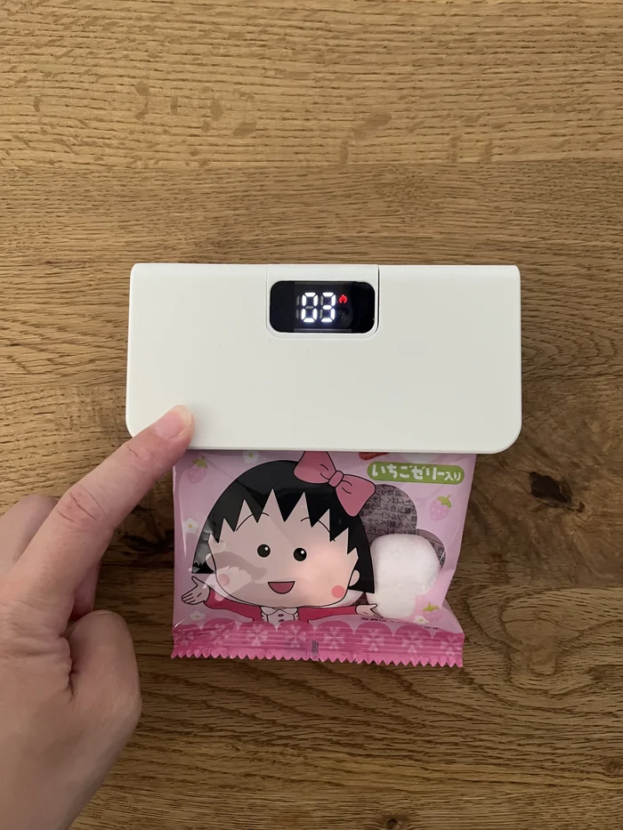 お菓子の袋を挟んだミニヒートシーラー。デジタル表示に残り秒数が表示されている