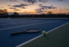 薄暮のハードコートに置かれたテニスラケットとテニスボールの情景