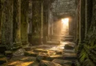 朝日が差し込む古代遺跡内部、苔むした石柱と謎めいた彫刻の壁