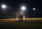 ナイター照明の下、ホームベース付近に集まる高校野球選手たちの歓喜のシルエット