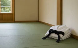 柔道場の畳の上に静かに置かれた柔道着と黒帯、しめやかな室内の情景