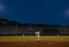 夜の高校野球場で打者が左翼方向へ打球を放つ後ろ姿、満員のスタンド