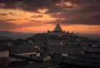 夕暮れの空にそびえる日本の城の天守閣と山並み、武家屋敷の甍