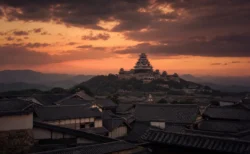 夕暮れの空にそびえる日本の城の天守閣と山並み、武家屋敷の甍