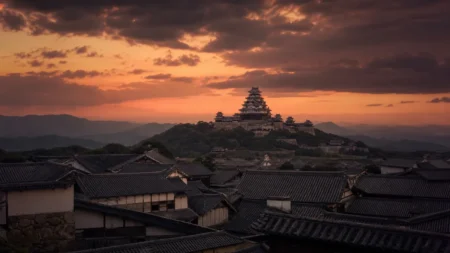 夕暮れの空にそびえる日本の城の天守閣と山並み、武家屋敷の甍