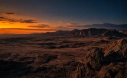 オレンジと紺のグラデーションに染まる荒野の夕景、岩山のシルエット