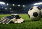 夜のスタジアム照明の下、芝生に置かれたゴールキーパーグローブとサッカーボール