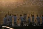 夕日を浴びるダグアウトで両手を上げて喜ぶ高校野球選手たちの後ろ姿