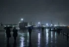 雨の夜の港湾エリアを傘をさして歩く人々のシルエット