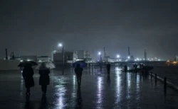 雨の夜の港湾エリアを傘をさして歩く人々のシルエット
