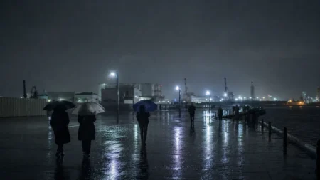雨の夜の港湾エリアを傘をさして歩く人々のシルエット