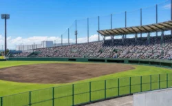 満員のスタンドが見える高校野球のスタジアム、昼間の強い日差しの中のグラウンド