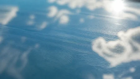 強い日差しの下で雲と青空を反射するガラス面