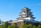 青空の下に佇む日本の城郭建築を思わせる写実的情景
