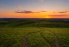 夕暮れ時の広大な草原と丘陵、細い小道が続く写実的な自然風景