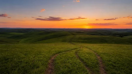 夕暮れ時の広大な草原と丘陵、細い小道が続く写実的な自然風景
