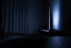 暗い部屋でテレビ画面の青白い光だけが漏れる深夜アニメ視聴の情景、手前にリモコンのシルエット