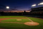 ナイター照明に照らされた無人の野球スタジアム、夕暮れの空とマウンド・ホームベース付近の芝生