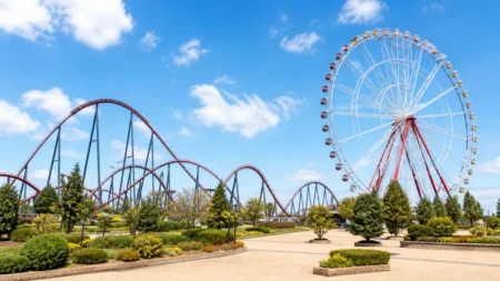 青空の下に観覧車とジェットコースターが並ぶ遊園地の情景