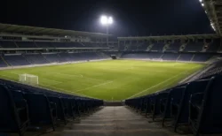 夜のサッカースタジアム、無人のスタンド席の通路から見下ろす芝生のピッチ、ナイター照明が柔らかく灯る情景