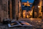 夕暮れのヨーロッパ旧市街の石畳の路地に置かれたレトロなフィルムカメラと開かれた写真集、奥に温かい灯りがともる歴史的な建物が並ぶ情景