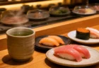 回転寿司店のカウンターに並ぶ湯呑みと数皿の寿司