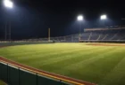 ナイター照明に照らされたプロ野球場の外野芝生とフェンス